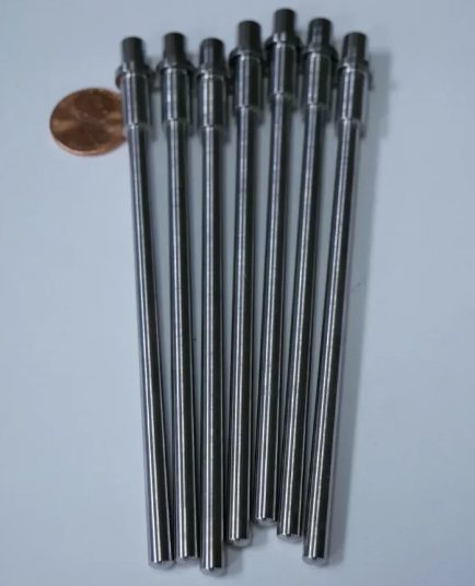 Long Swiss machined pins with penny for scale – Chesapeake CNC